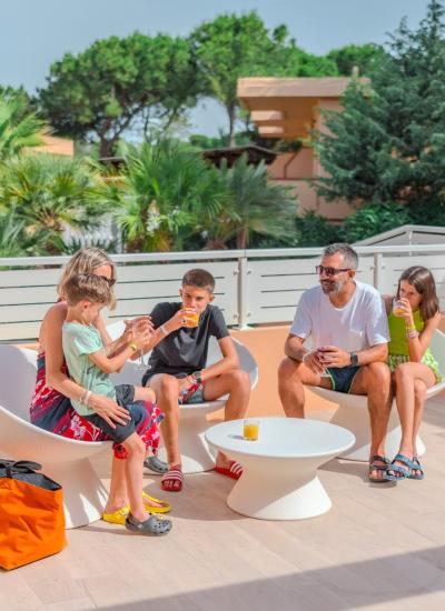 Family drinks juice on sunny terrace, surrounded by trees.