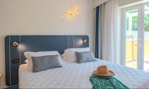 Helles Zimmer mit Doppelbett, Hut und Sommerkleid.