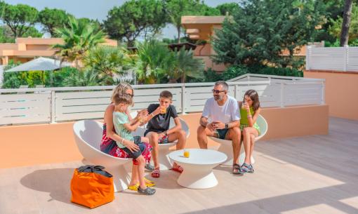 Family drinks juice on sunny terrace, surrounded by trees.