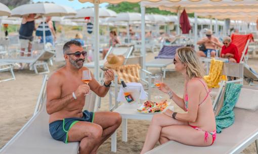 Couple toasting at the beach with wine and fruit.