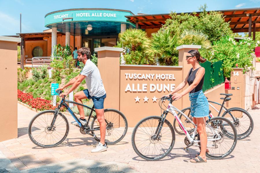 Couple cycling in front of Tuscany Hotel Alle Dune, four stars.